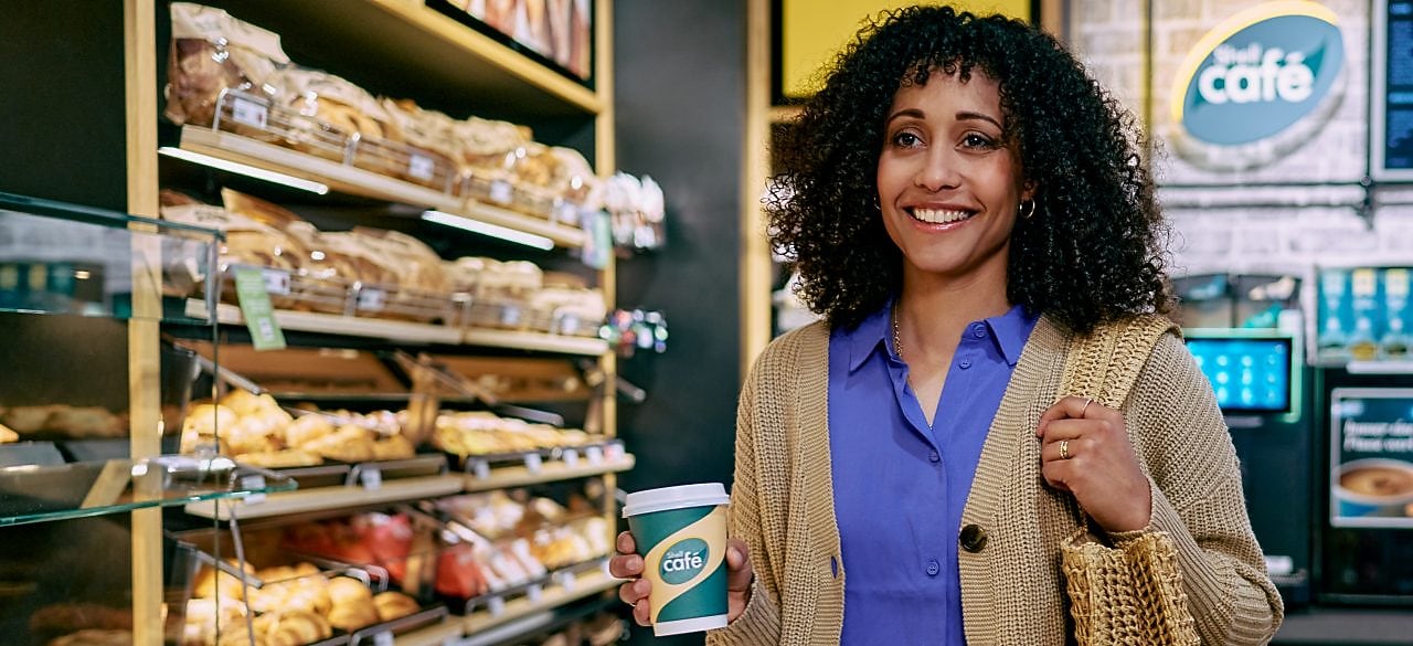 Une femme souriante avec un café de Shell Café à une station Shell dotée d’une boulangerie Shell Café