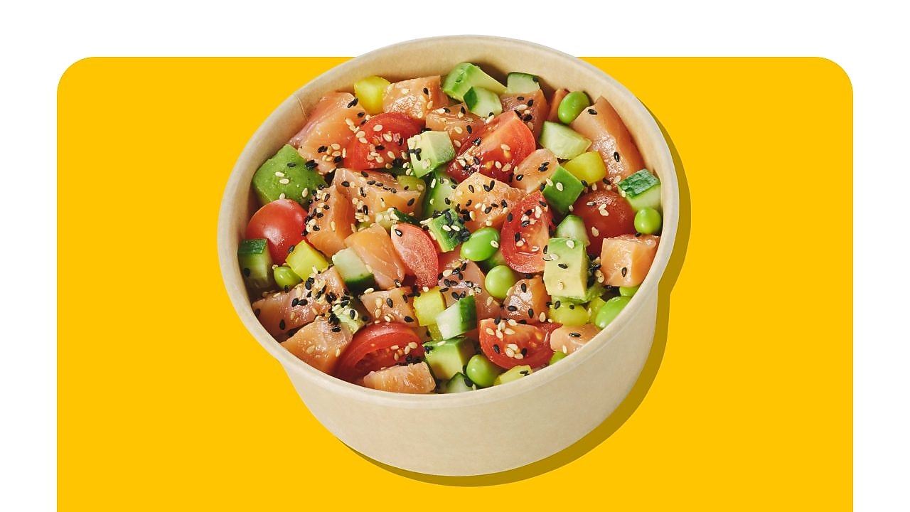 Poke Bowl classique au saumon vu d’en haut avec ingrédients frais tels que saumon, edamames, avocat, mangue et tomates sur fond jaune.