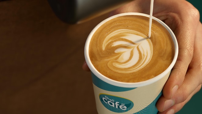 Un barista sert un café au lait dans un gobelet Shell Café