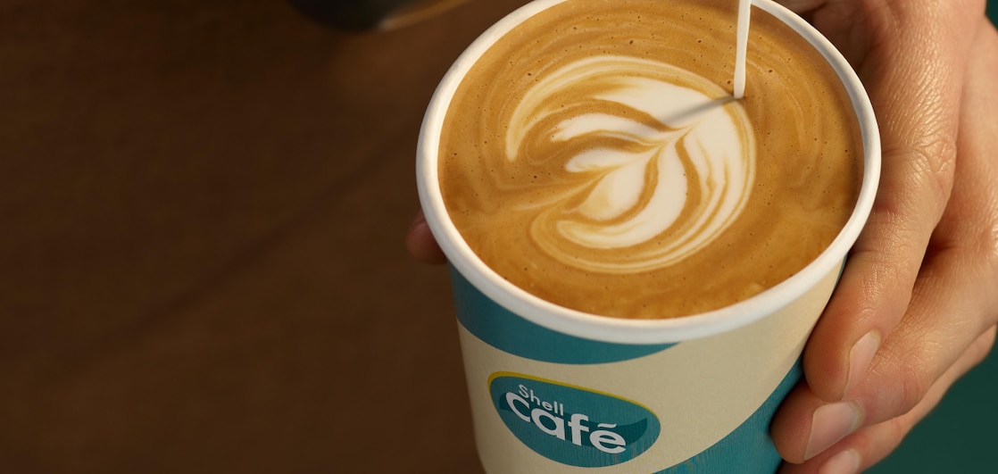 Un barista sert un café au lait dans un gobelet Shell Café