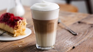 Un latte macchiato de Shell Café servi dans un verre haut posé sur une table en bois.
