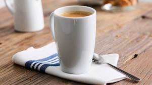 Café allongé servi dans un gobelet en porcelaine Shell Café posé sur une table en bois