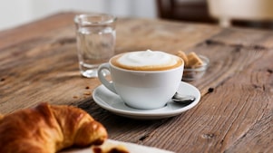 Un cappuccino dans une tasse en porcelaine Shell Café posé sur une table en bois